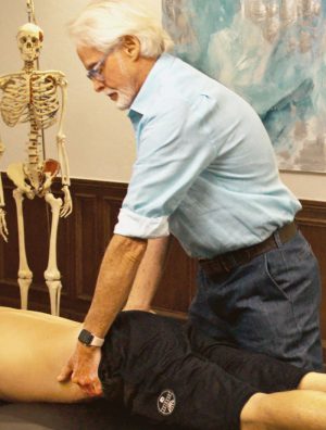 Image 6. Iliosacral Alignment Technique: The therapist's left hand lifts the client's left anteriorly/inferiorly rotated ilium and his right palm braces the right posterior superior iliac spine. The therapist gently pulls with his left hand while resisting with his right. The client is asked to gently push his left ilium toward the table to a count of five and relax. The therapist rotates the client's pelvis to the next restrictive barrier to restore Z-join alignment.